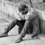 man in gray jacket and black pants sitting on concrete bench